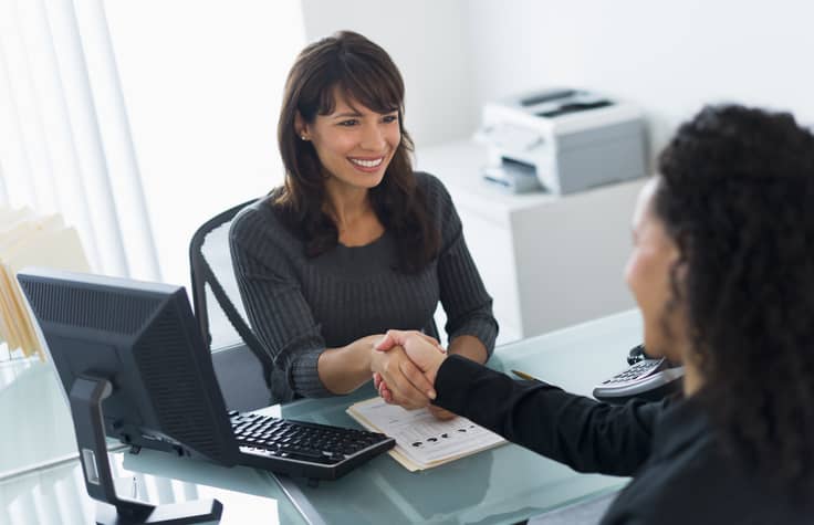 Hiring manager shaking the hand of a new employee in an office.